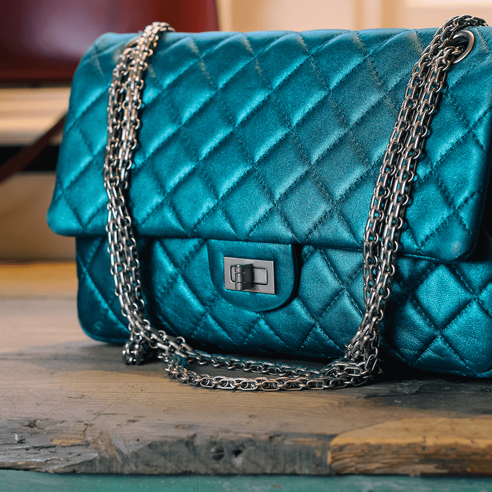 Shiny blue quilted Chanel bag with silver chain on a wooden table in a vintage boutique.