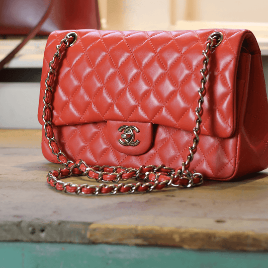 Preloved red quilt Chanel handbag with chain strap, sitting on an antique wooden table in a vintage boutique.